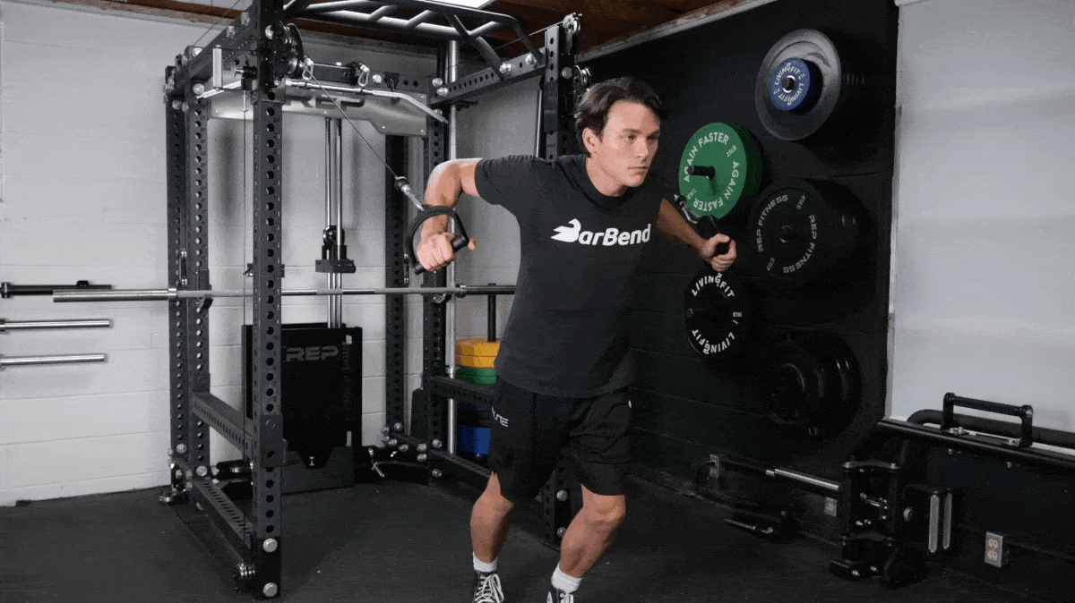 Man in a grey t-shirt that reads "BarBend" on it performs cable flyes in a power rack.