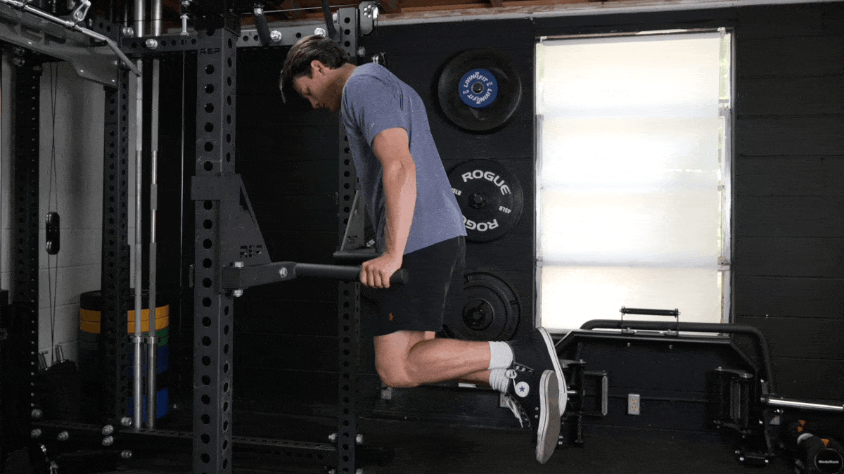 Person in a grey t-shirt and black shorts performs dips on using bars attached to a power rack.