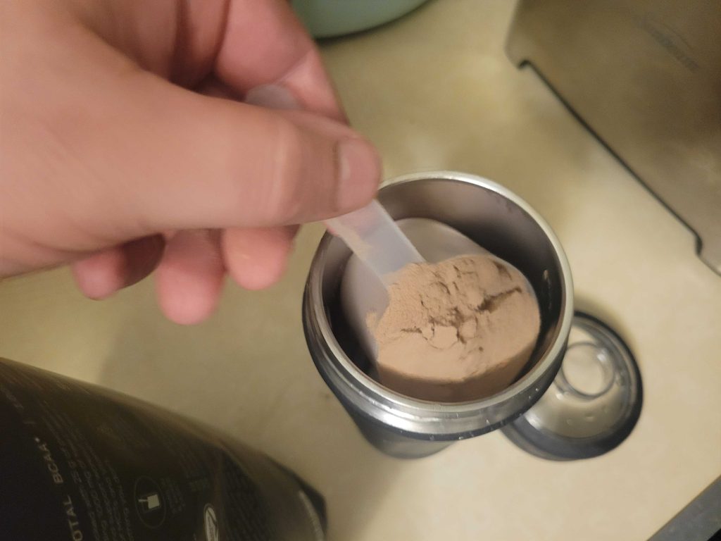 Our tester dumping a scoop of Sports Research Whey Protein Isolate into a shaker bottle.