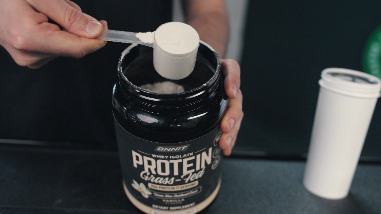 Scoop of Onnit Whey Isolate Protein Powder is held just above the opened container