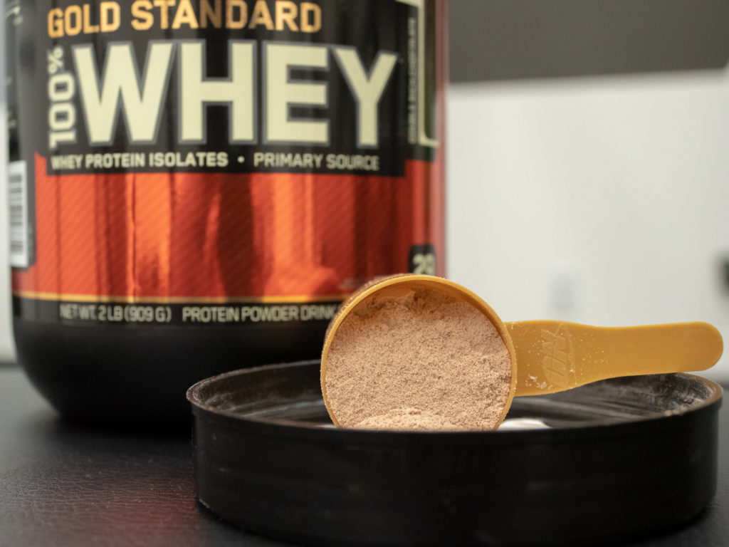 A scoop of Optimum Nutrition Gold Standard rest on the lid of the container