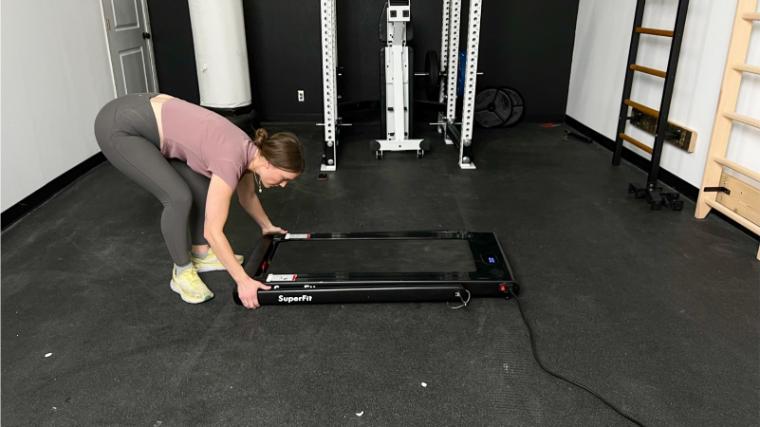 Our tester in a gym reaches down grabbing the handle bar on a SuperFit Treadmill.