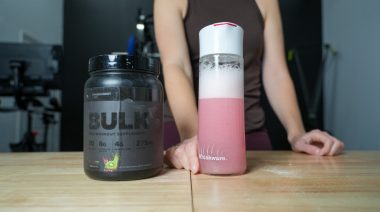 A woman stands behind a shaker glass and container of Transparent Labs Bulk Black Pre.