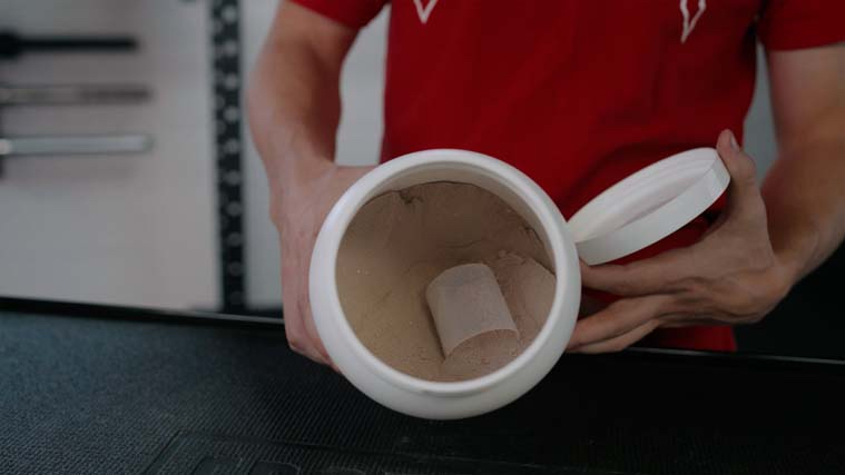 A person holding an open container of Transparent Labs Whey Isolate Powder so the inside is visible