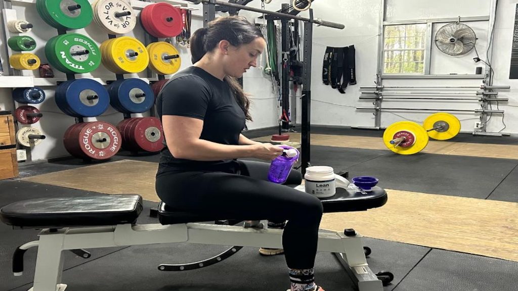 A person sits on a weight bench and mixes Transparent Labs LEAN.