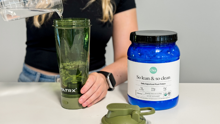 A person pours water into a blender next to Ora Organic Protein.