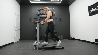 A woman walks at a slight incline on a manual treadmill.