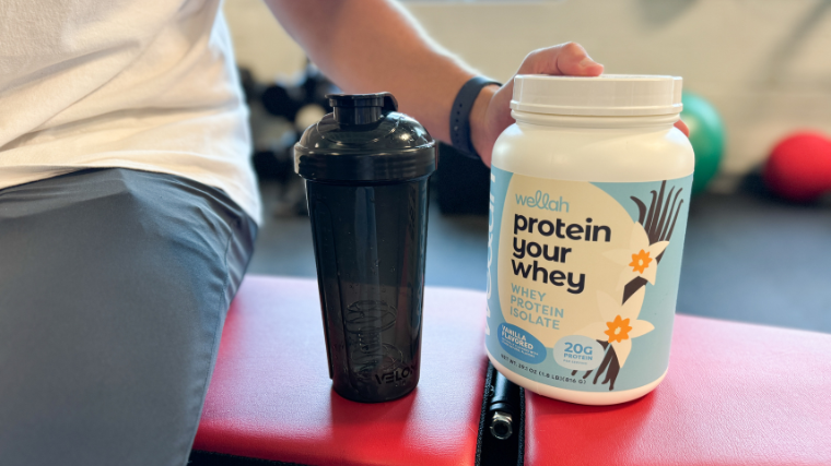 A person displays a tub of Wellah Protein Your Whey.